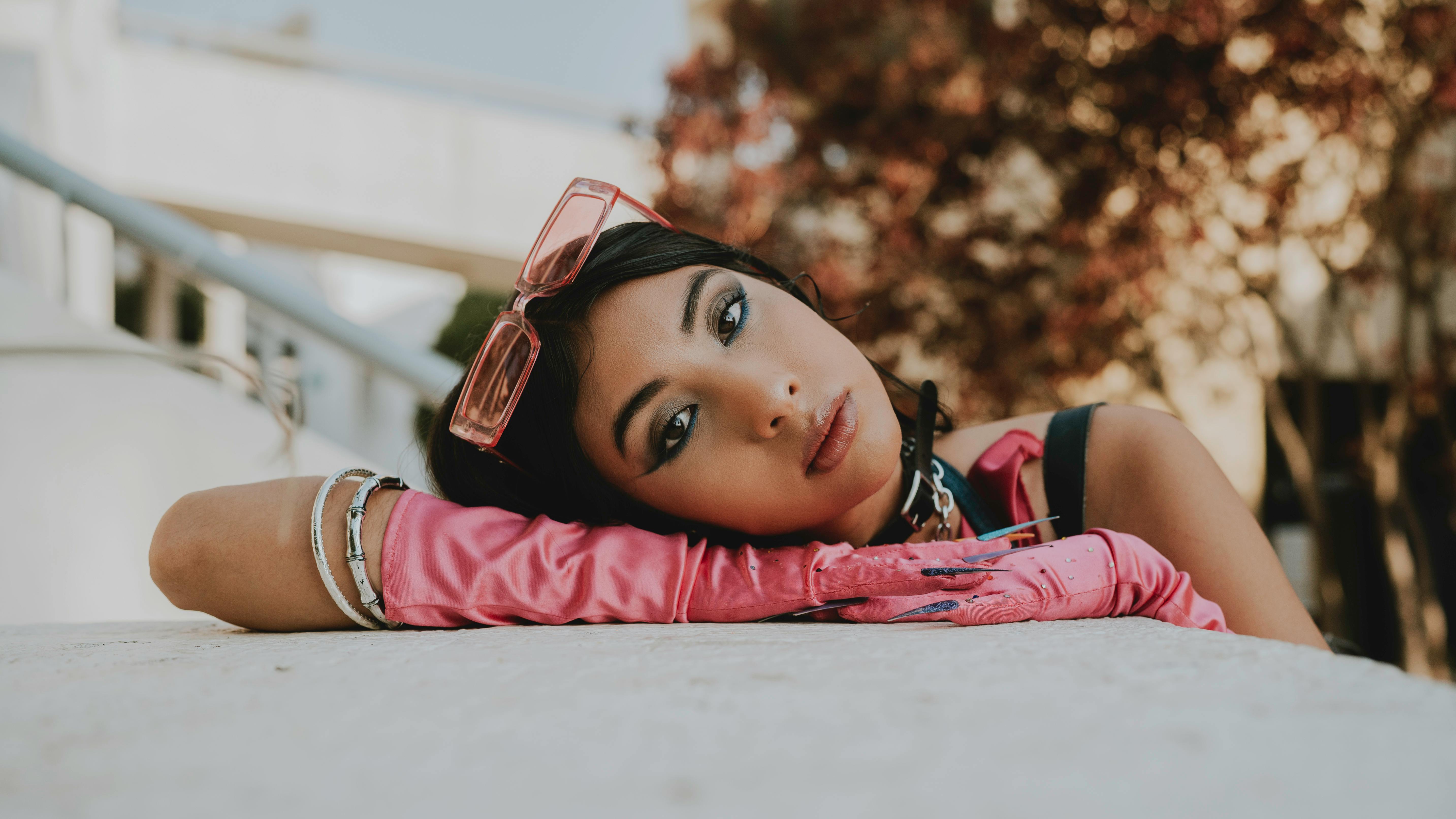 girl with pink gloves leaningon her arm with pink transluscent sunglasses outside by a staircase