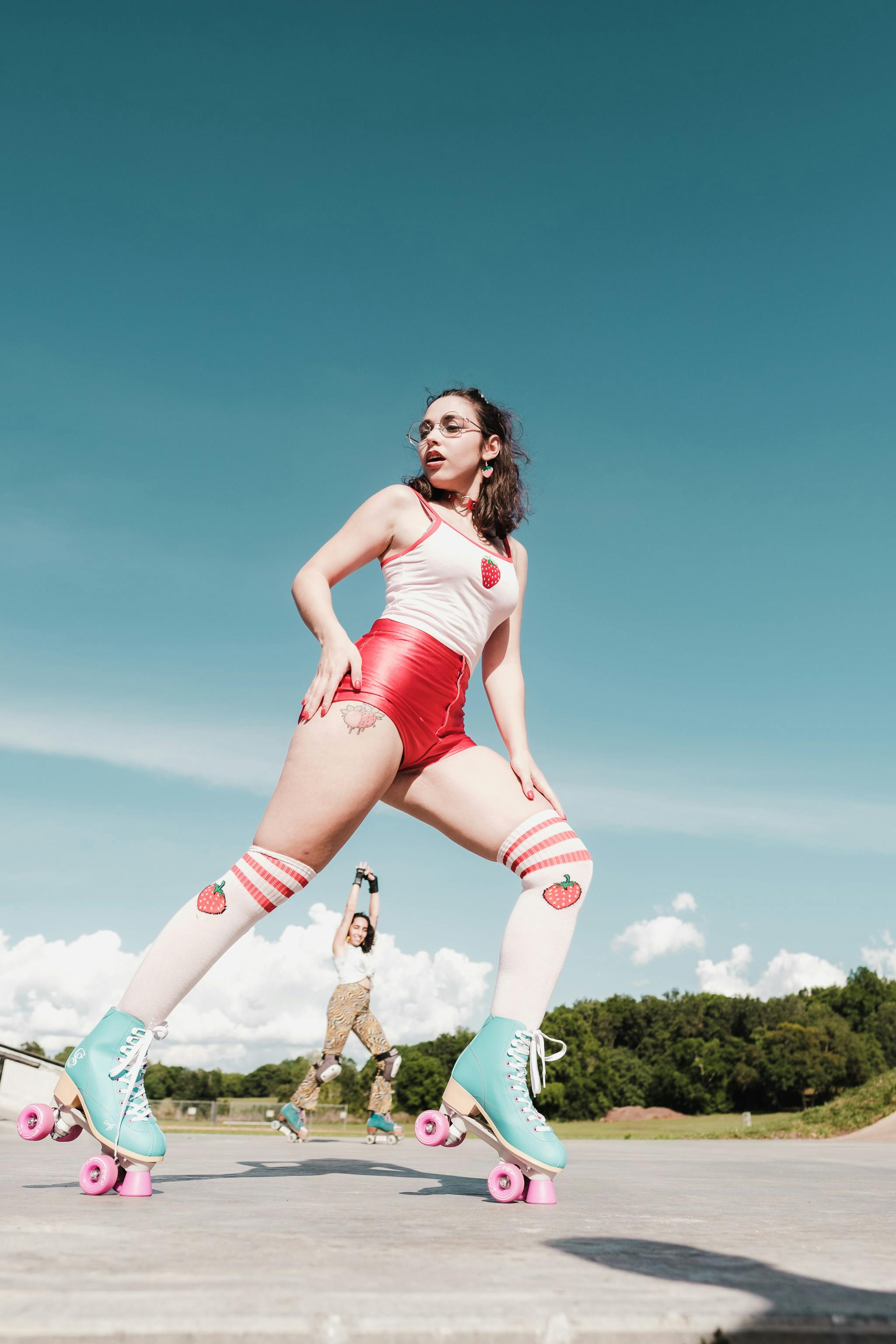 Girl in a strawberry top and socks and red shorts and blue skates and pink wheels on a bright day with blue sky